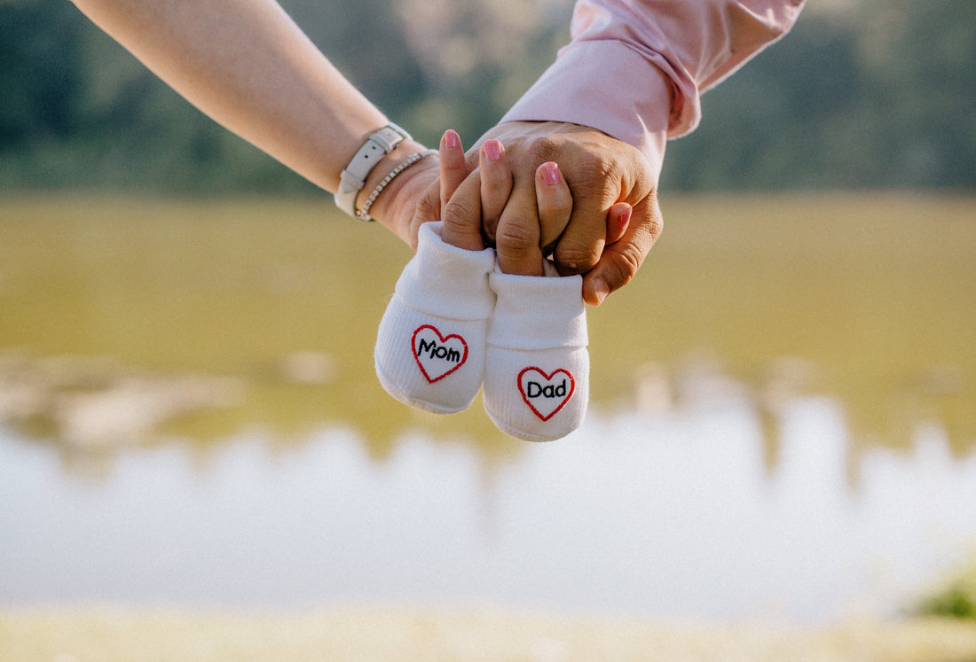 Pregnancy announcement showcasing parents holding hands and a small pair of socks that read "Mom and Dad".