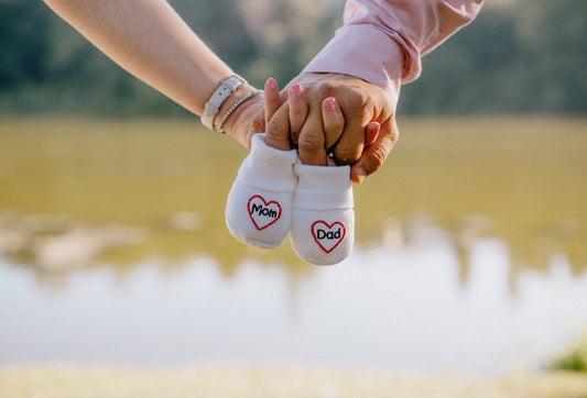 Pregnancy announcement showcasing parents holding hands and a small pair of socks that read "Mom and Dad".